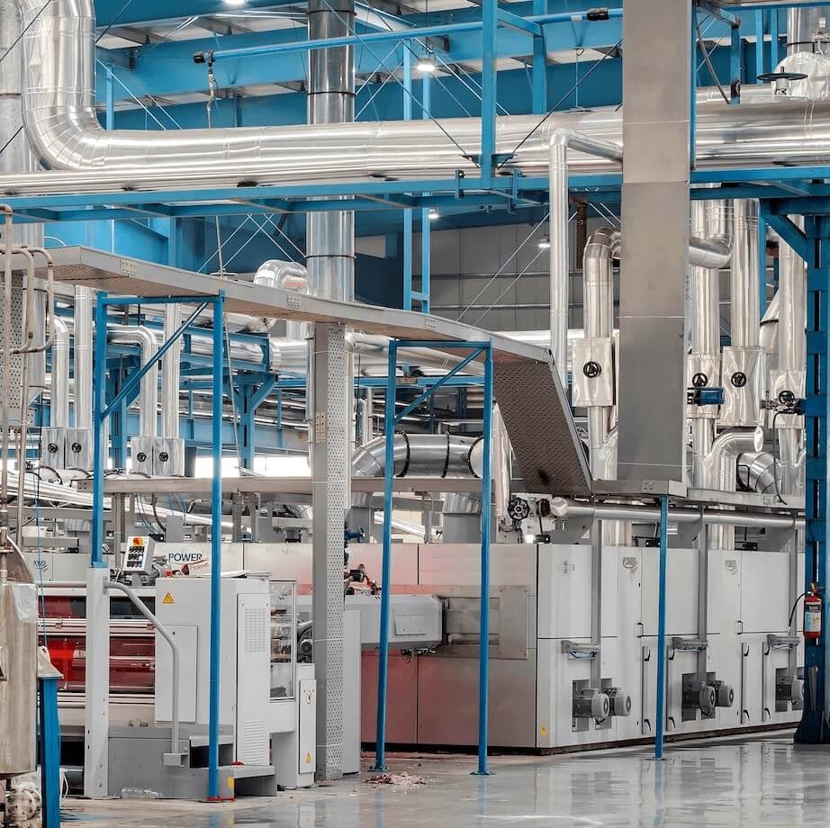 Interior view of the Axxion manufacturing facility, featuring large industrial machinery, silver ventilation pipes, and blue steel framework used to produce factory-direct wholesale paper products.