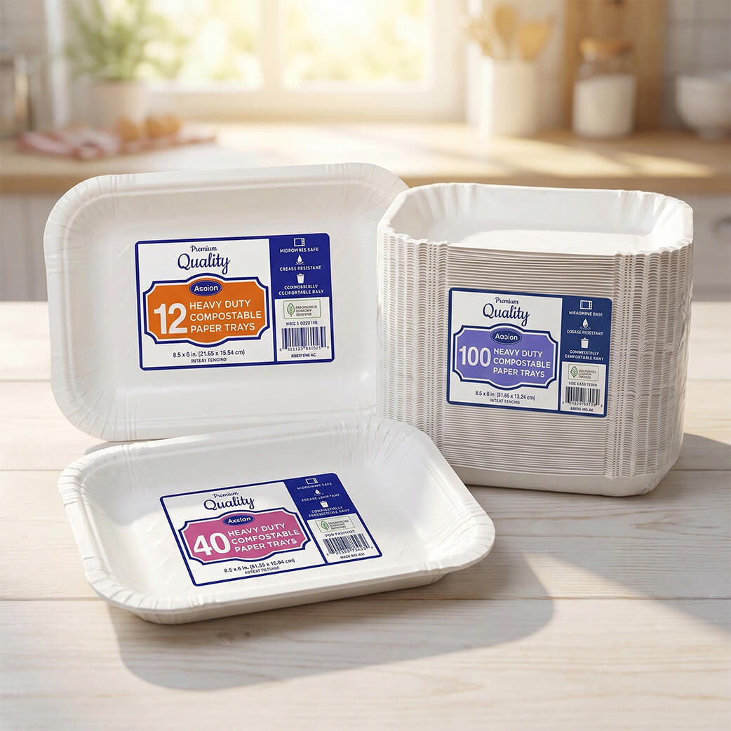 Bulk packages of Axxion premium heavy-duty white paper food trays resting on a light wooden countertop in a sunlit kitchen setting. Disposable serving trays available in high-count bundles, ideal for wholesale restaurant supplies, catering, and food trucks.